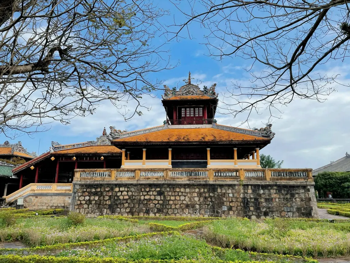 An imperial pavilion framed by bare branches in Huế